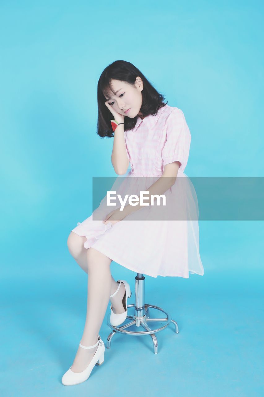 Young beautiful woman sitting on chair against blue background