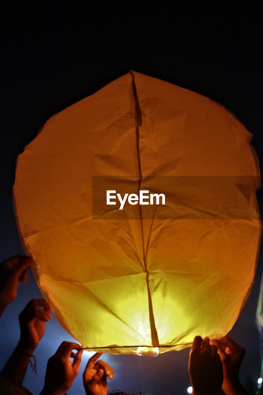 Low angle view of hands holding sky lantern at night