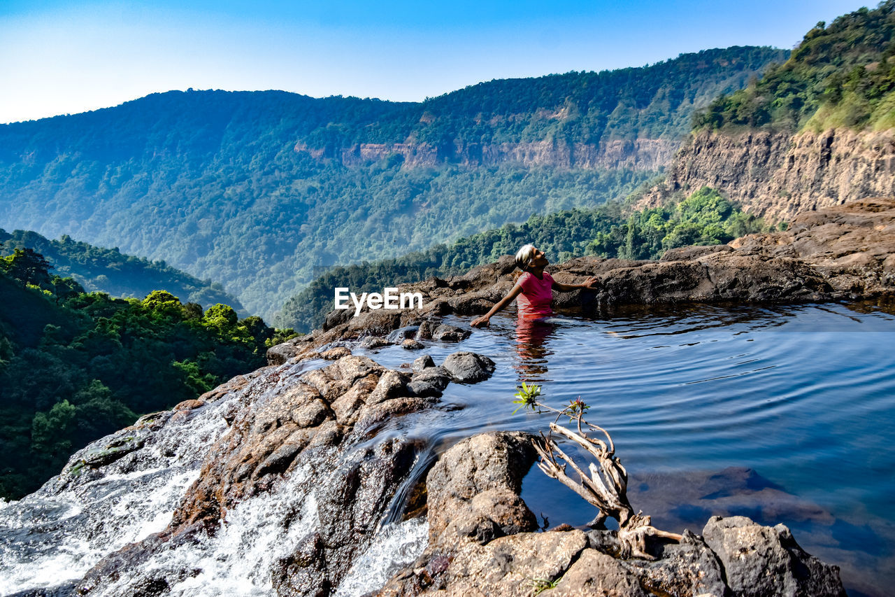 Woman standing on rock by mountain against sky