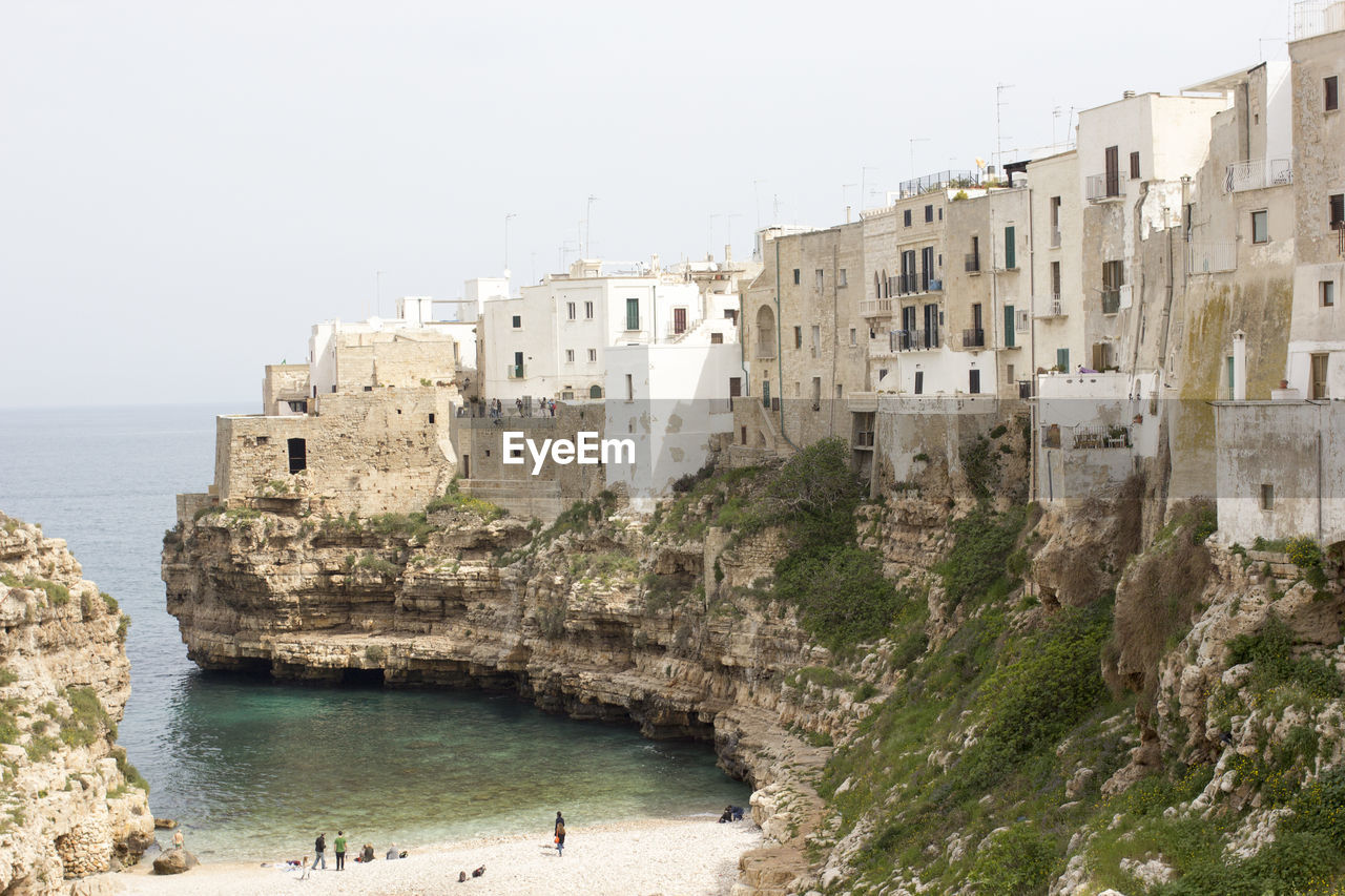Buildings on cliff by sea at polignano a mare against sky