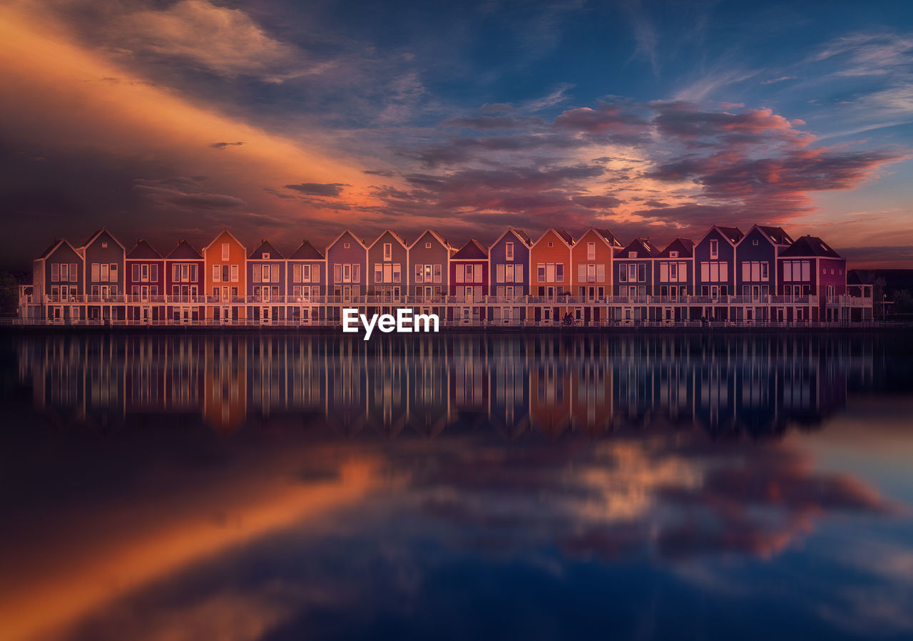 Reflection of buildings on lake against sky during sunset