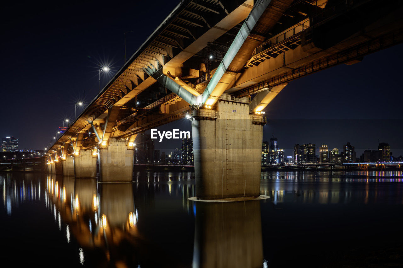 illuminated bridge over river in city at night