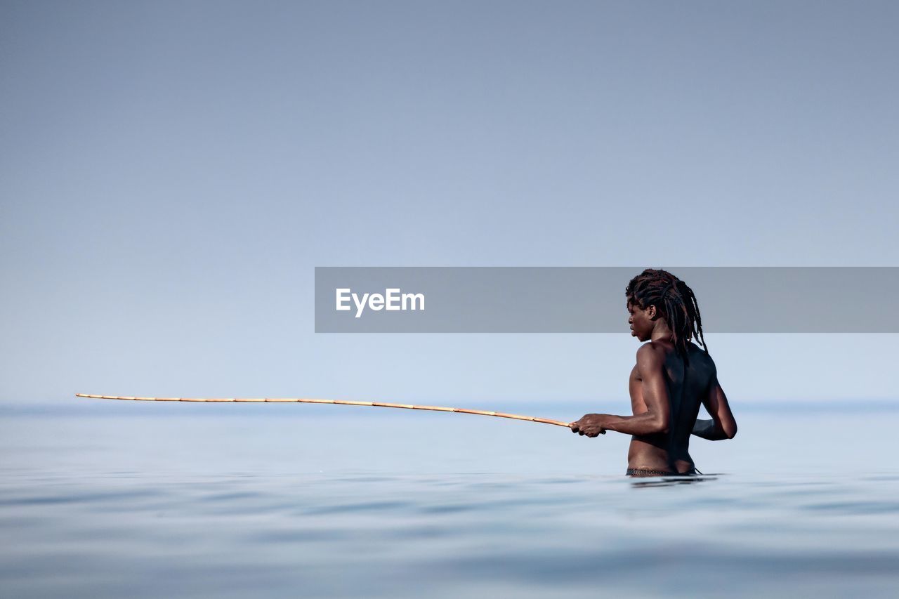 Shirtless man holding stick in sea