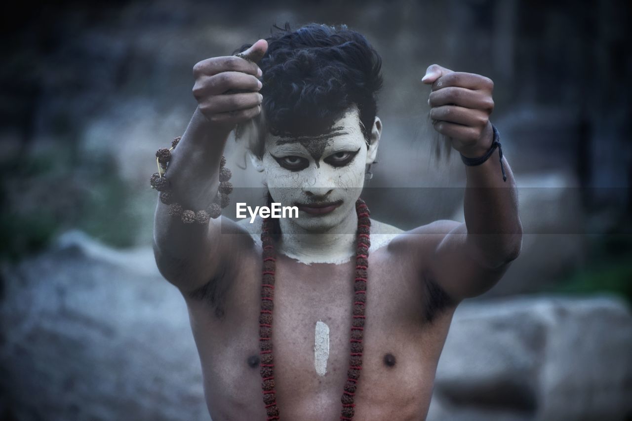 Portrait of serious young man with face paint pouring soil 