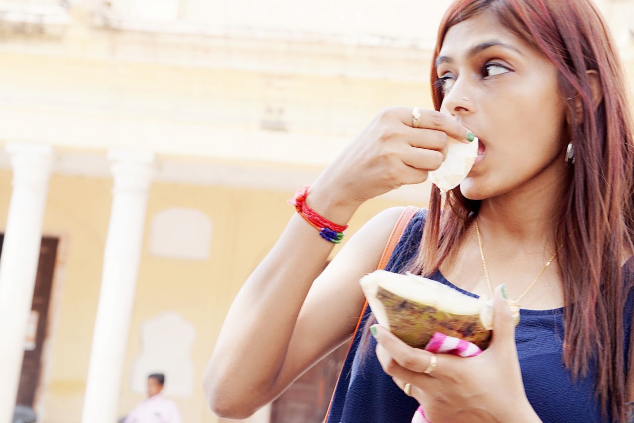 Low angle view of young woman eating coconut while standing on street