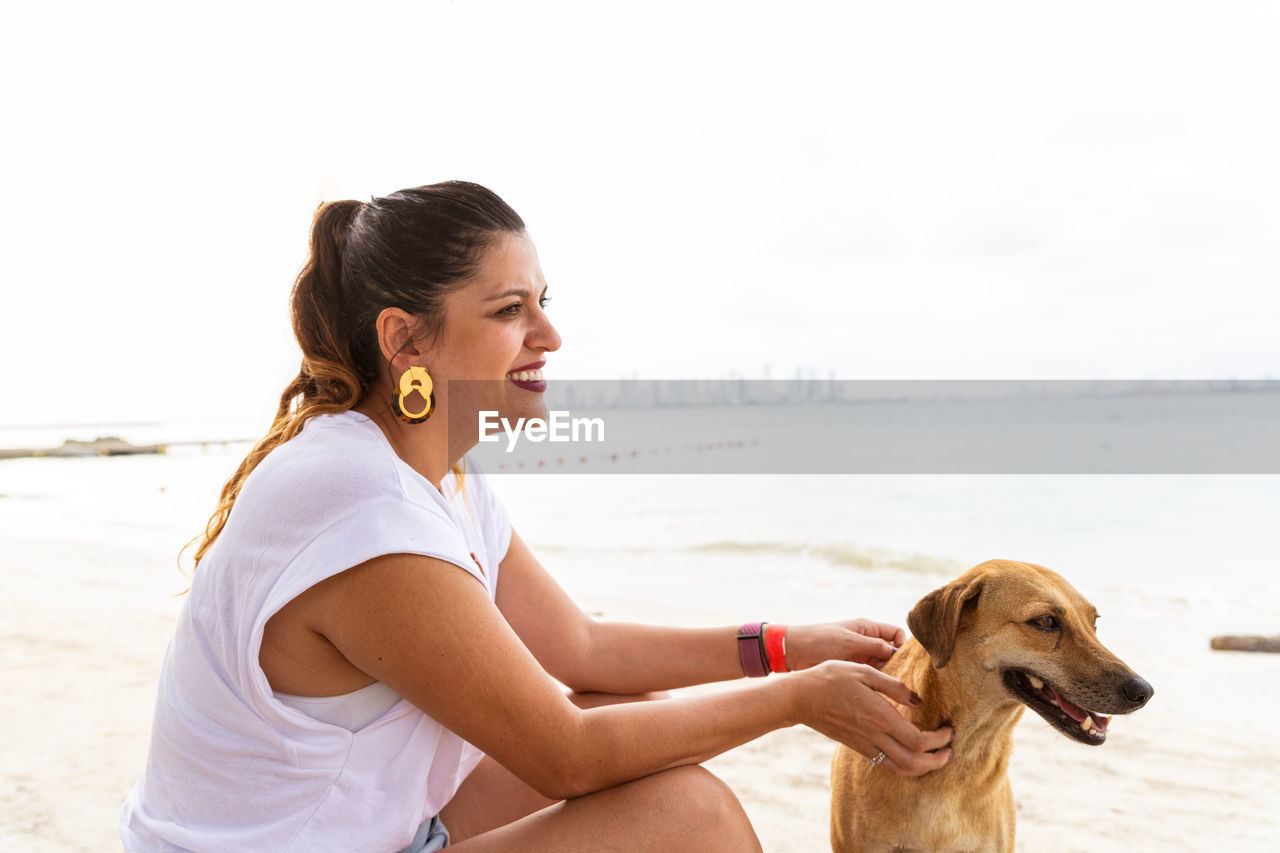 side view of young woman sitting on beach against clear sky