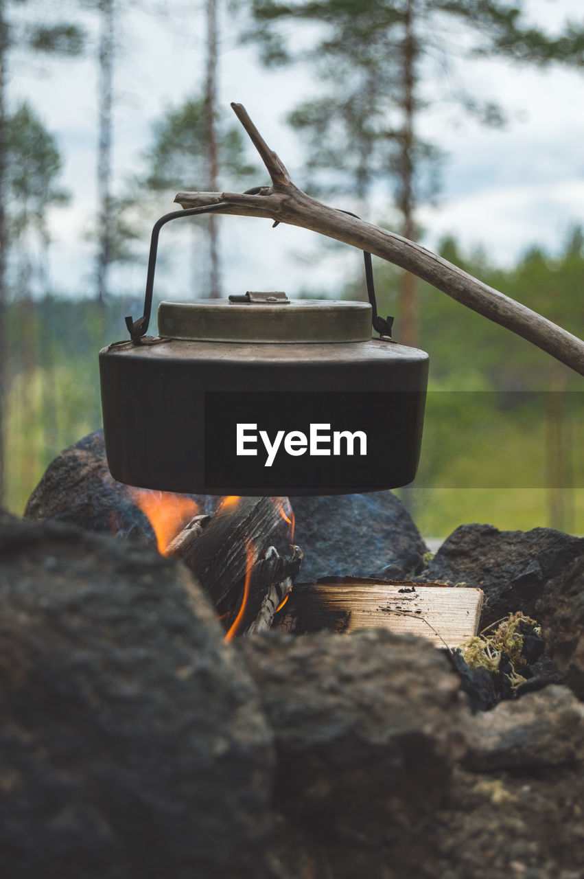 Close-up of container hanging on stick over campfire