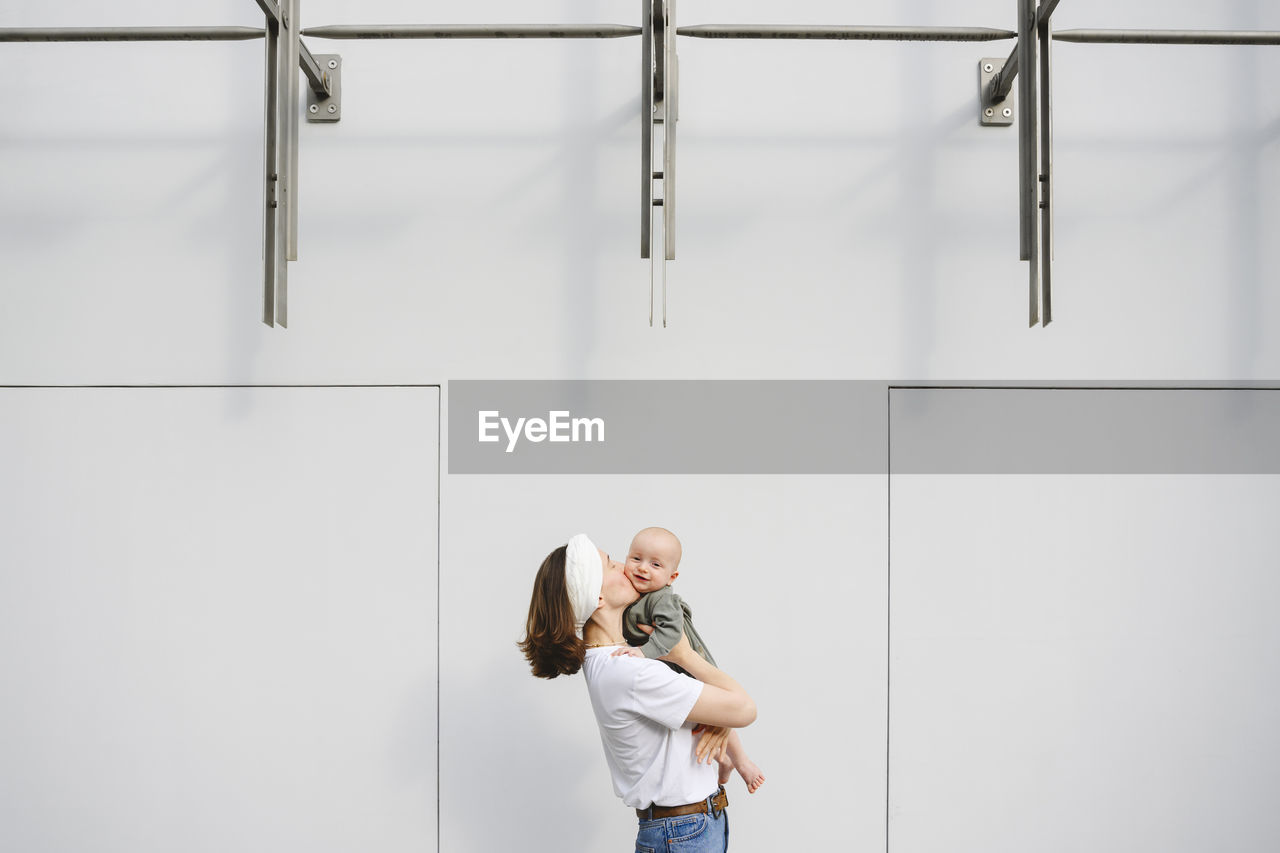 Mother kissing baby boy in front of wall