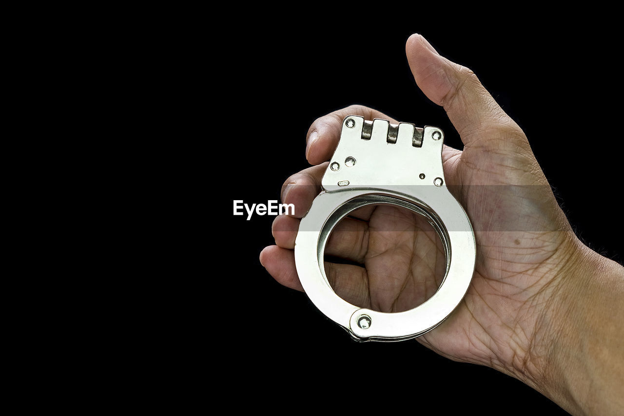 Cropped image of hand holding handcuffs against black background