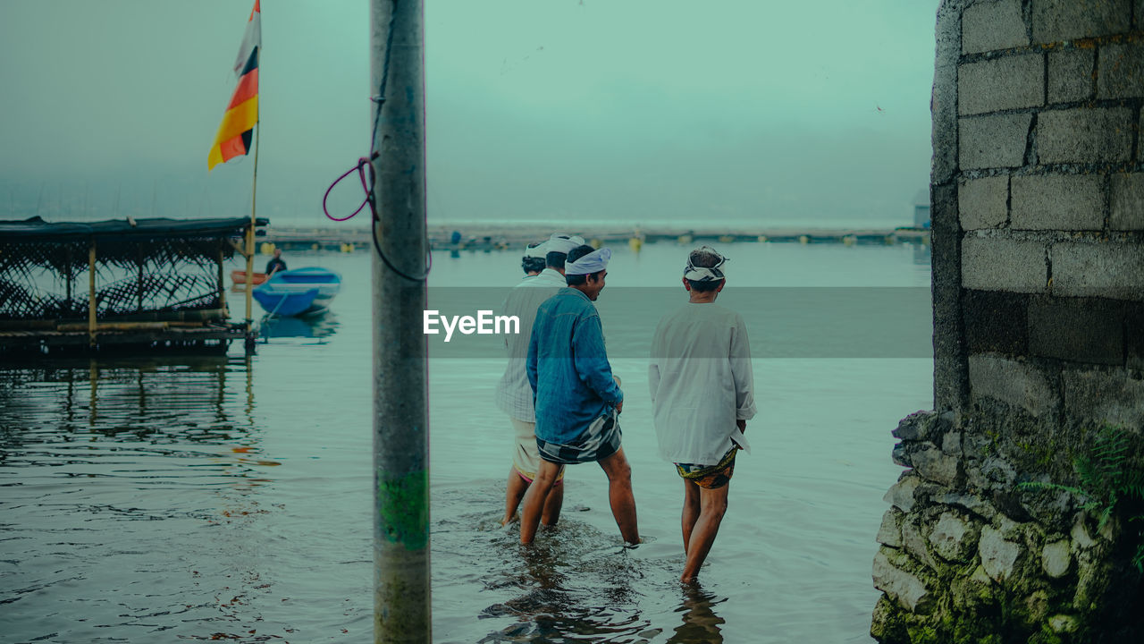 Rear view of men standing at beach against sky