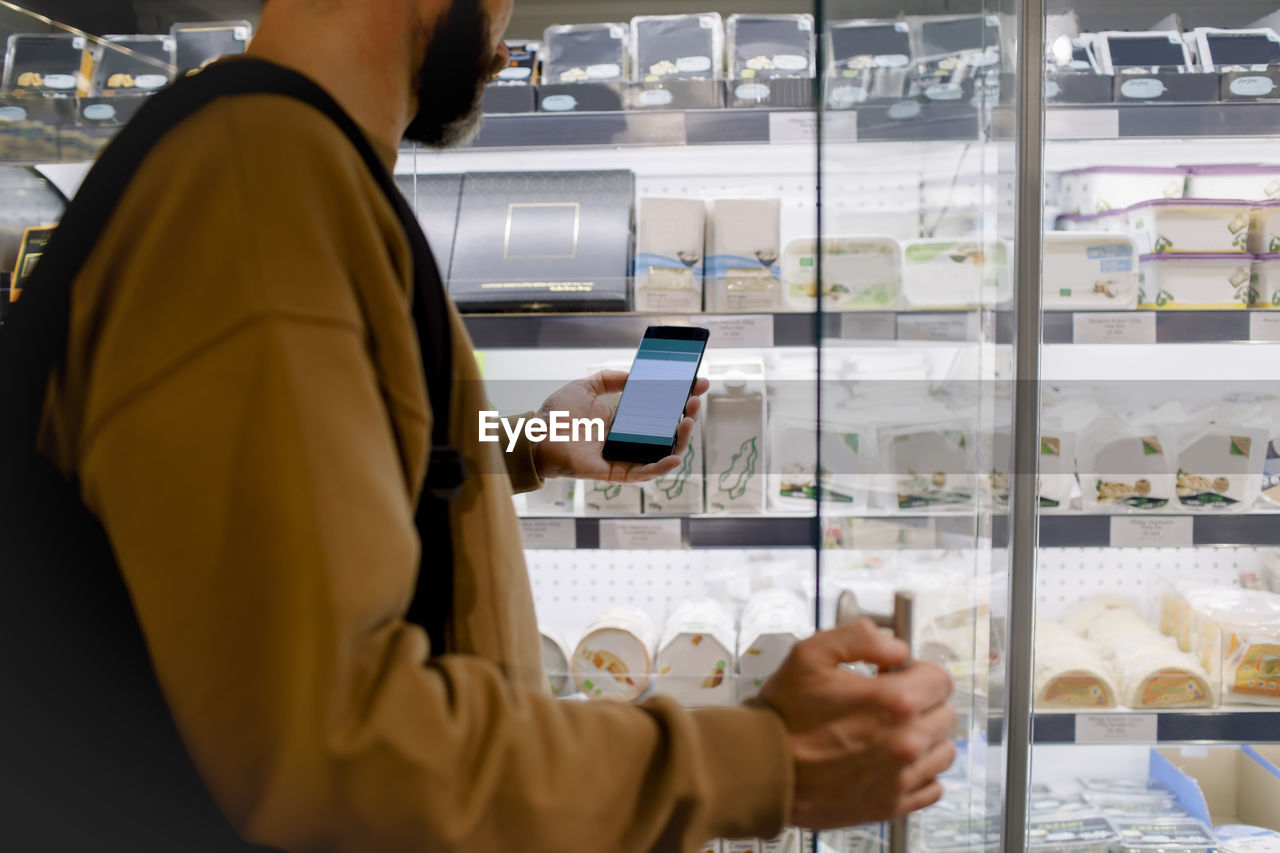 Midsection of male customer using smart phone while shopping in supermarket