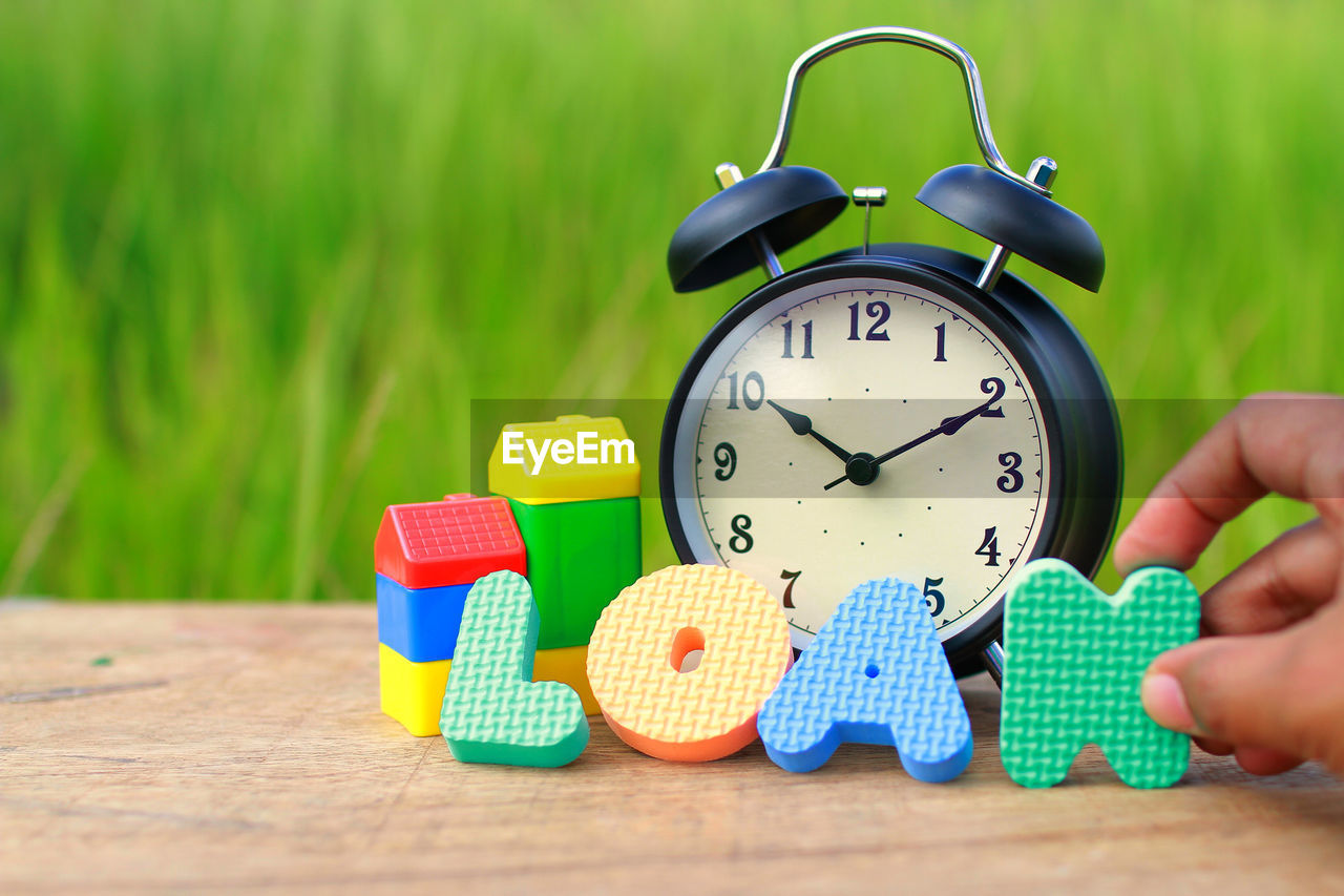 Cropped hand holding alphabet by alarm clock on table