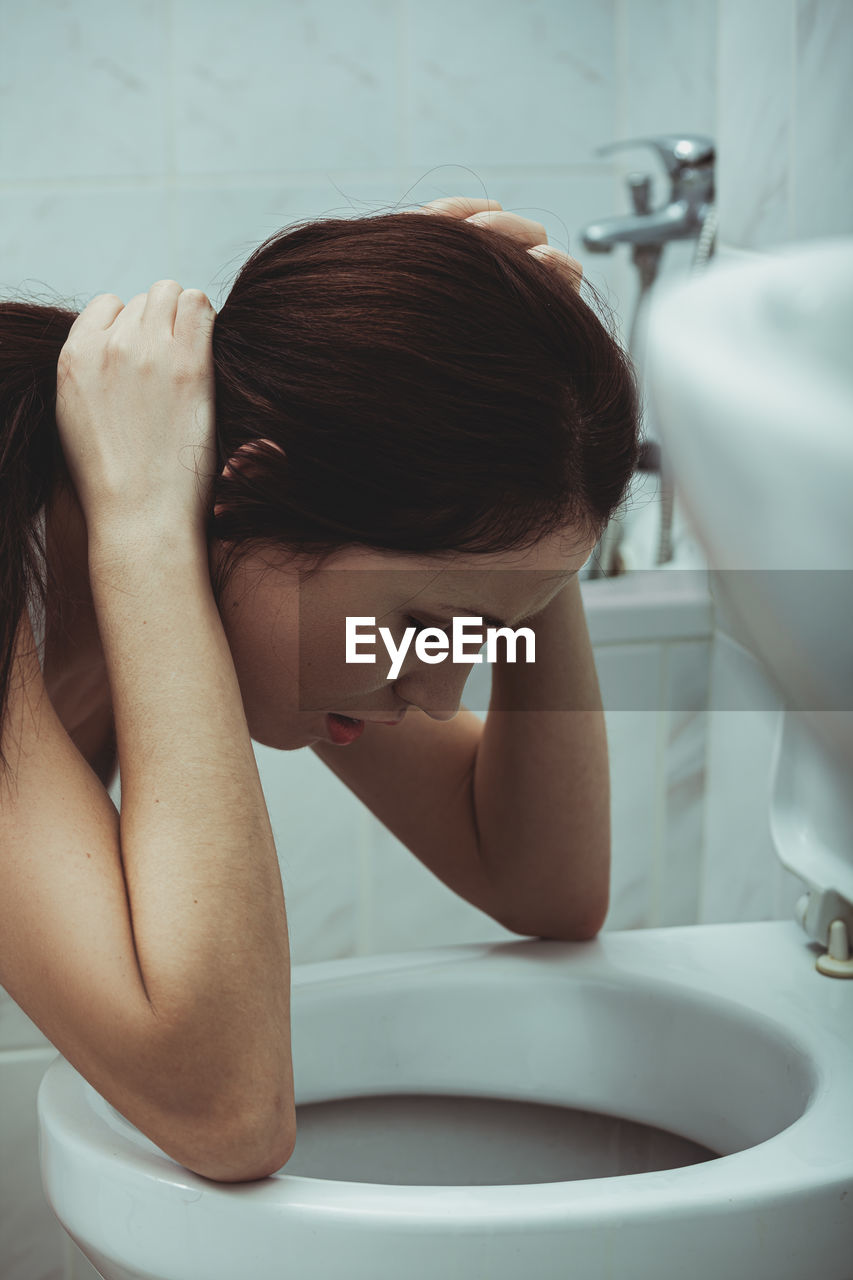 Woman vomiting in toilet bowl