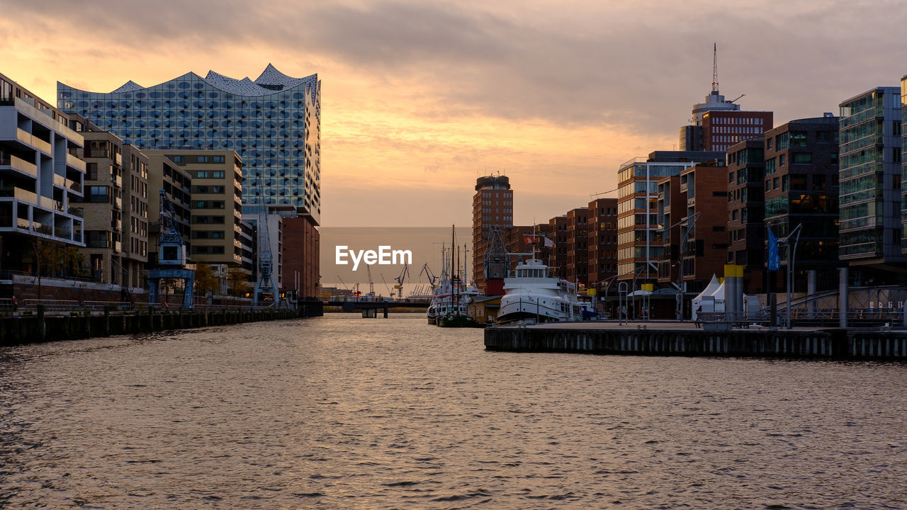 SEA BY BUILDINGS AGAINST SKY DURING SUNSET