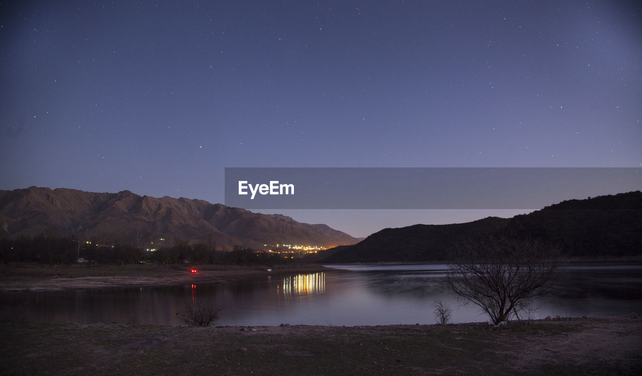 Scenic view of lake by mountains against star field