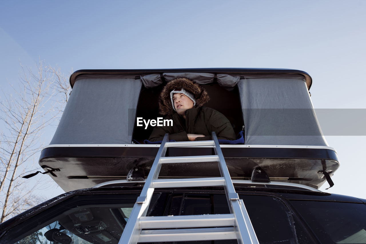 Low angle view of man sitting in roof tent on car