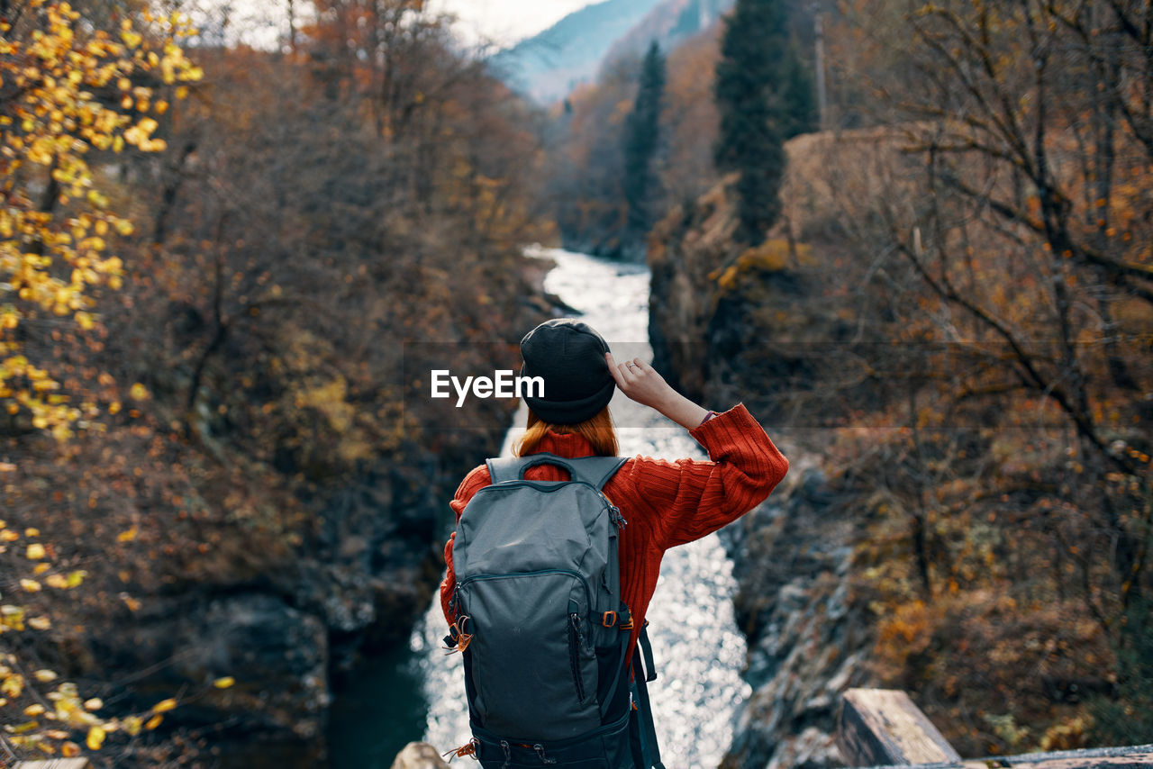 REAR VIEW OF MAN STANDING AT FOREST DURING AUTUMN