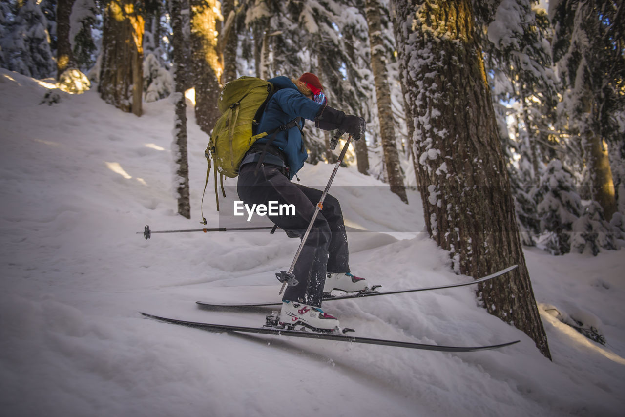 Woman skiing down between trees at sunset in the backcountry