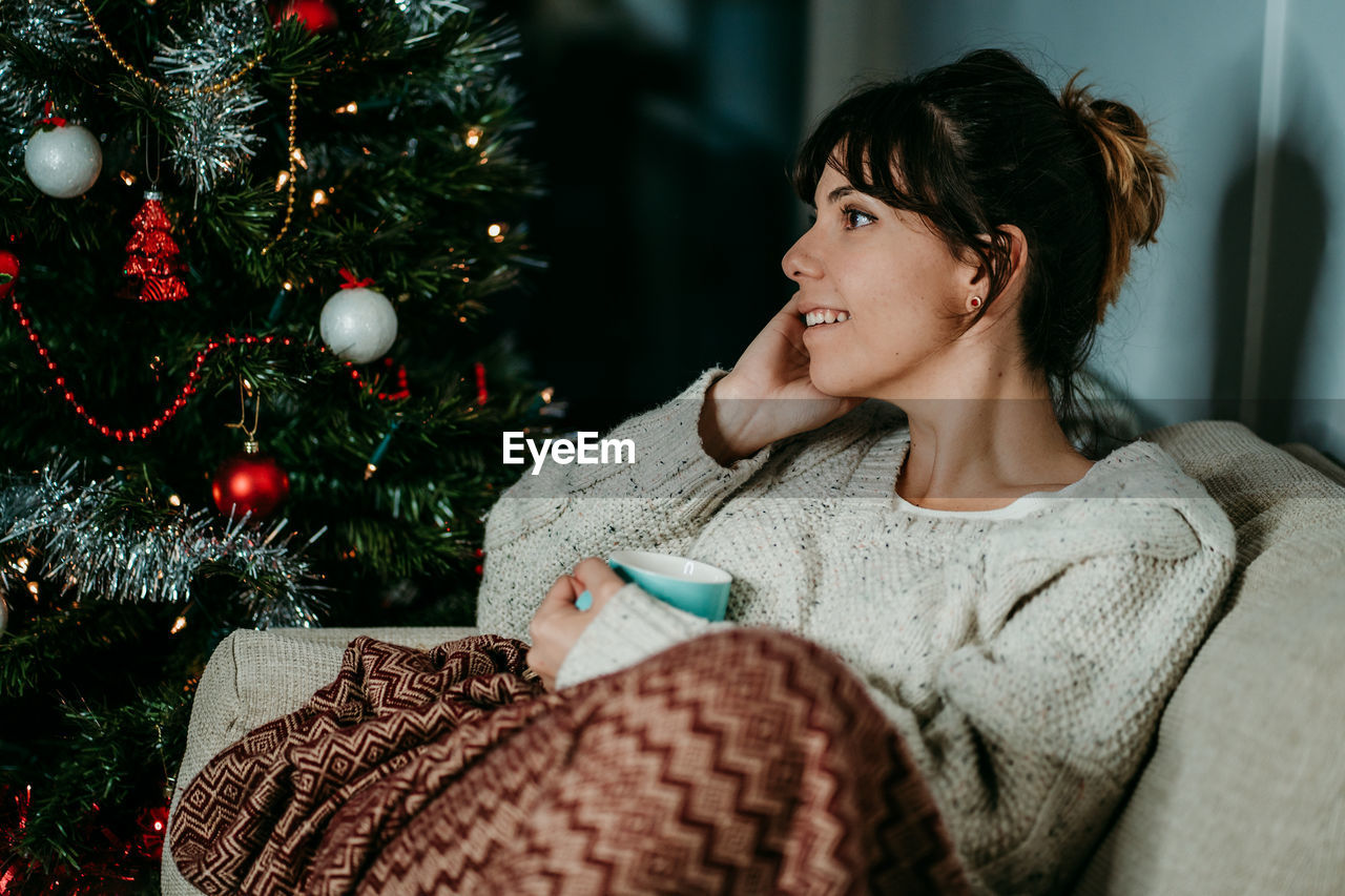 Portrait of young woman standing by christmas tree at home