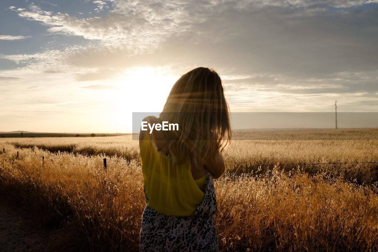 Woman standing on dry grassy field during sunset