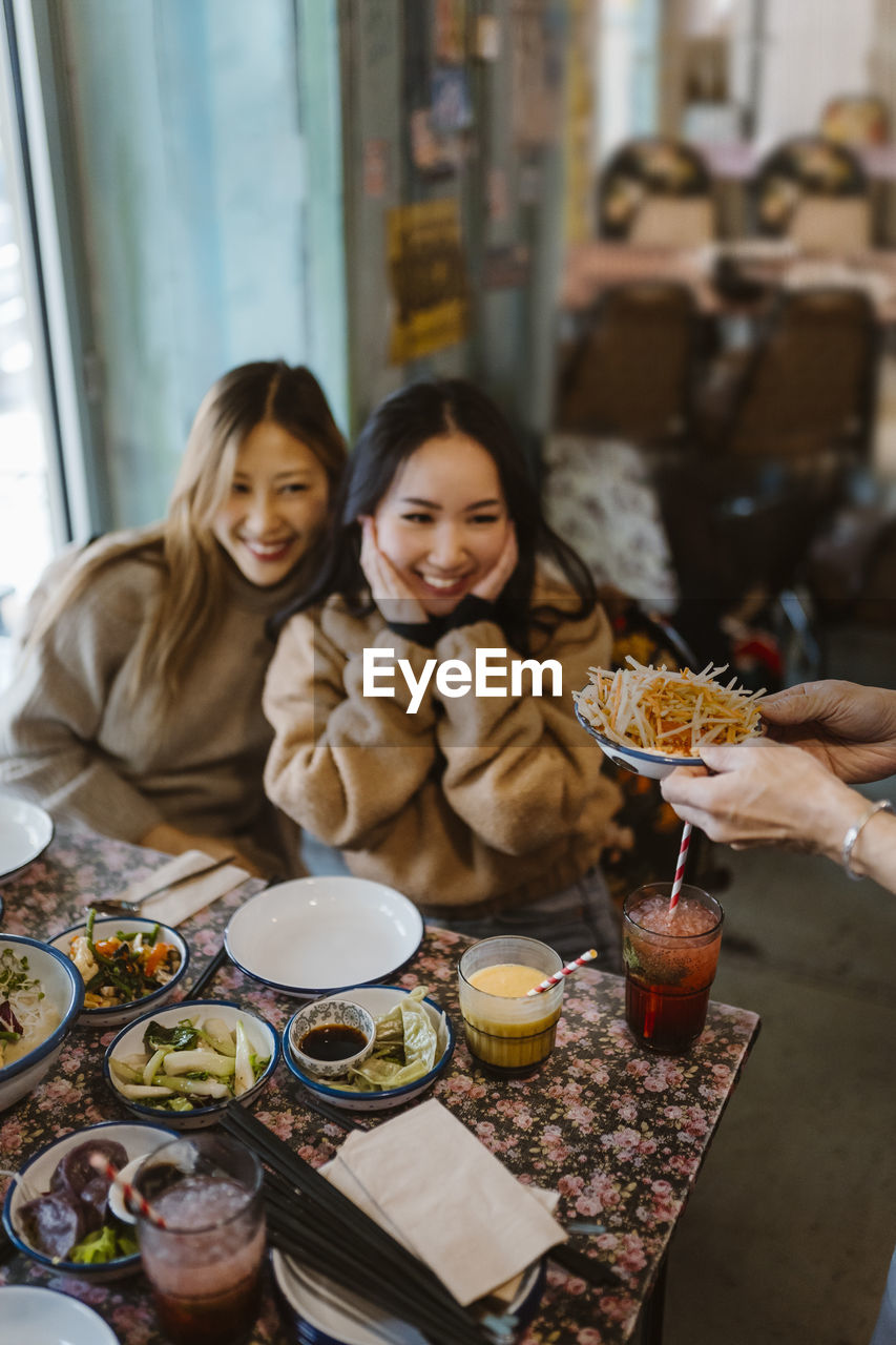 Happy female friends looking at food being served at restaurant