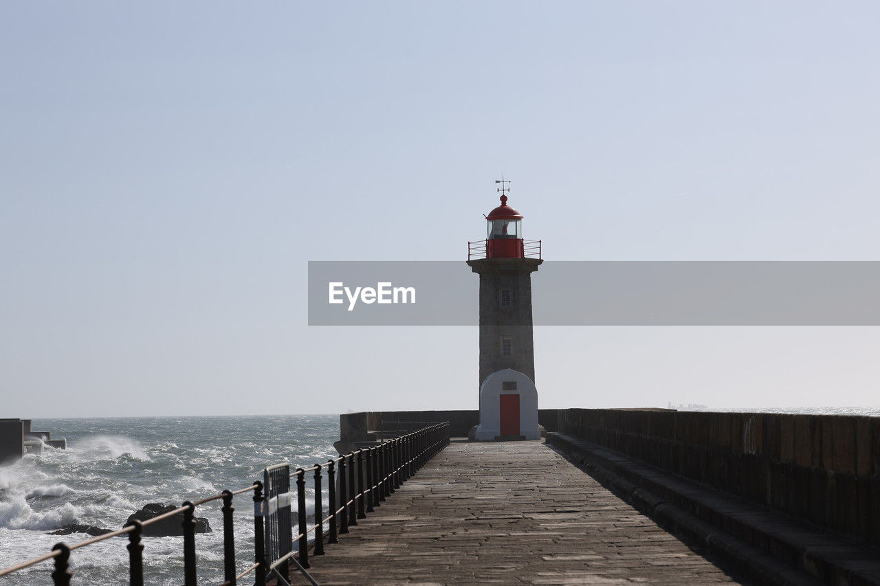 lighthouse, guidance, architecture, sea, water, built structure, sky, security, tower, protection, building exterior, coast, beach, walkway, nature, building, clear sky, horizon over water, horizon, boardwalk, ocean, travel destinations, pier, land, railing, breakwater, day, no people, scenics - nature, coastline, the way forward, travel, outdoors, tranquility, copy space, beauty in nature, jetty, tranquil scene, history, sunny, the past, environment, sunlight, non-urban scene, footpath, tourism, transportation, wood, urban skyline, landscape