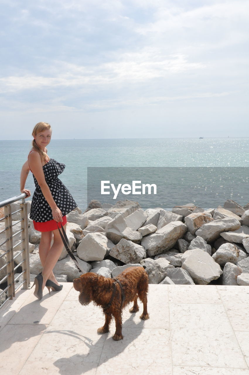 Portrait of woman with dog standing by sea against sky