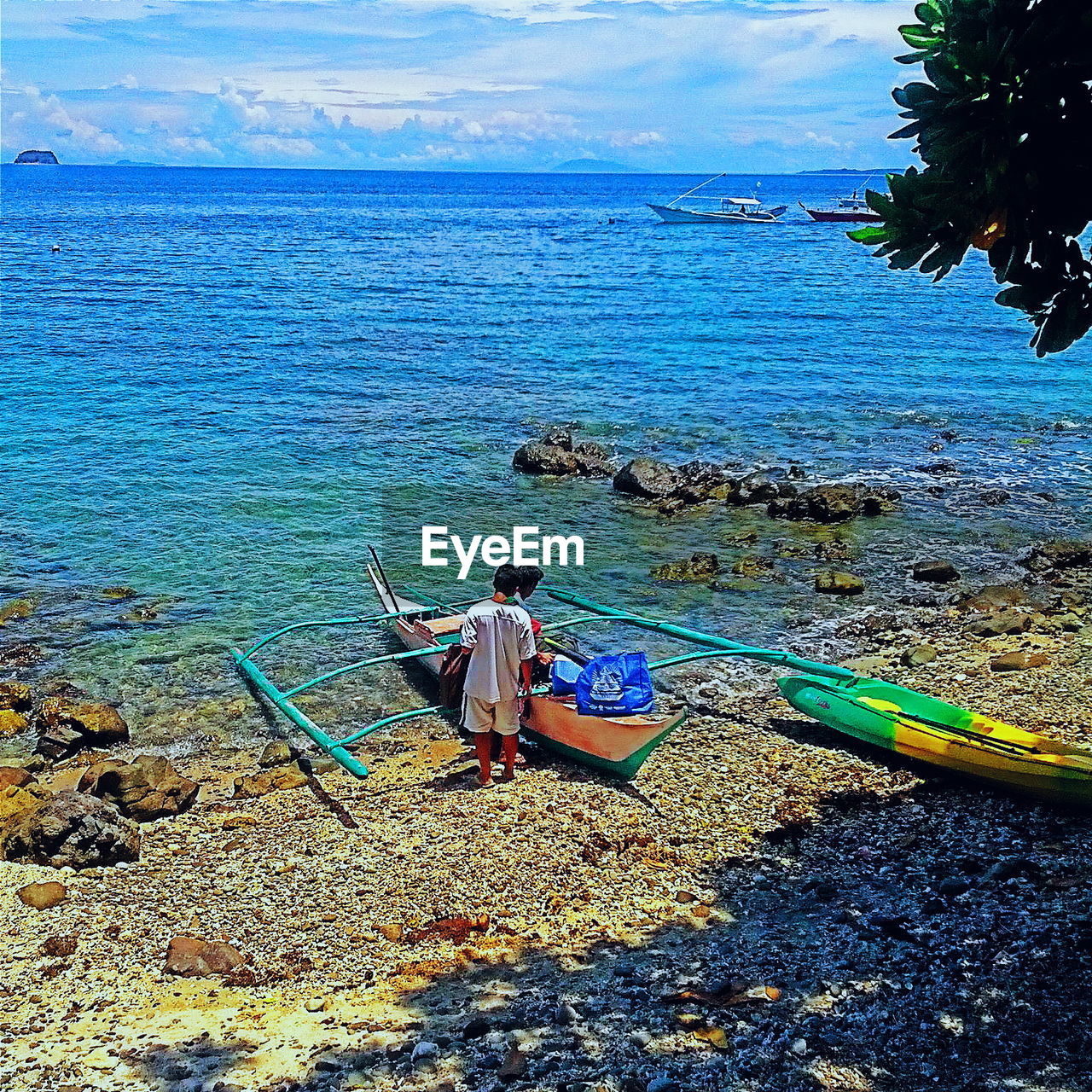 Rear view of men standing by outrigger canoe at sea shore against cloudy sky