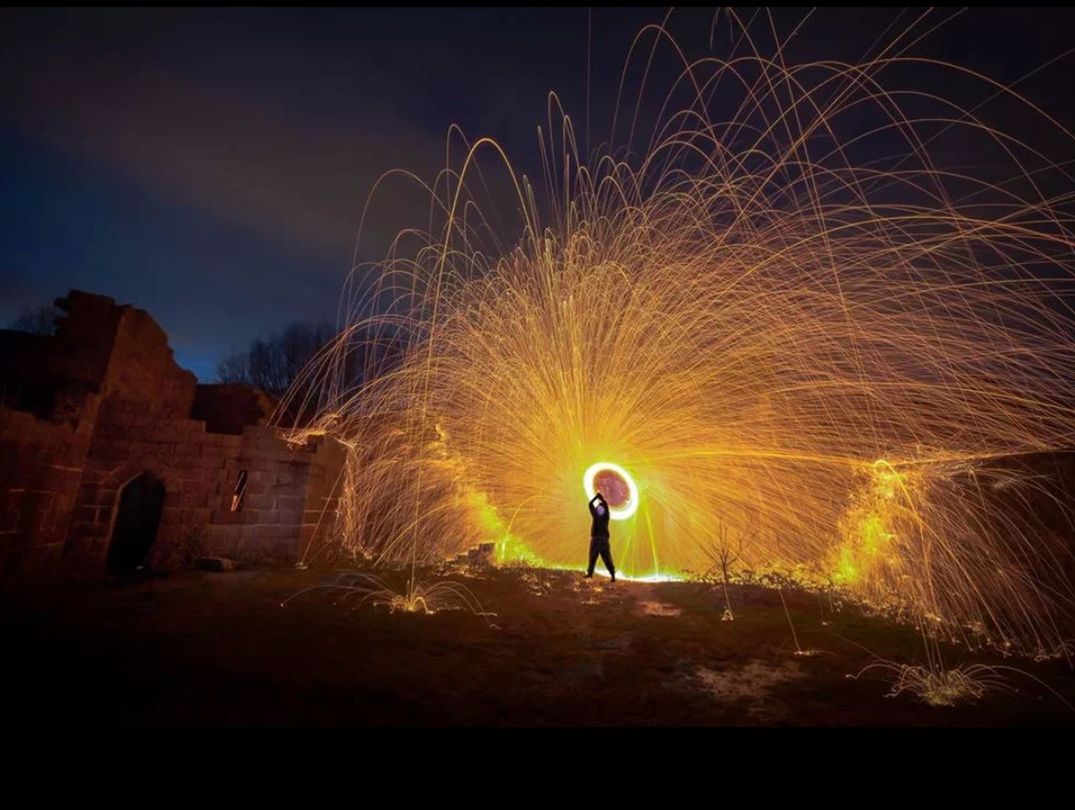 Silhouette man spinning illuminated wire wool at night