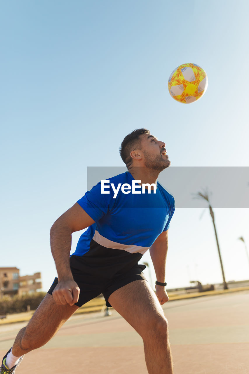 Man heading ball while playing soccer during sunny day
