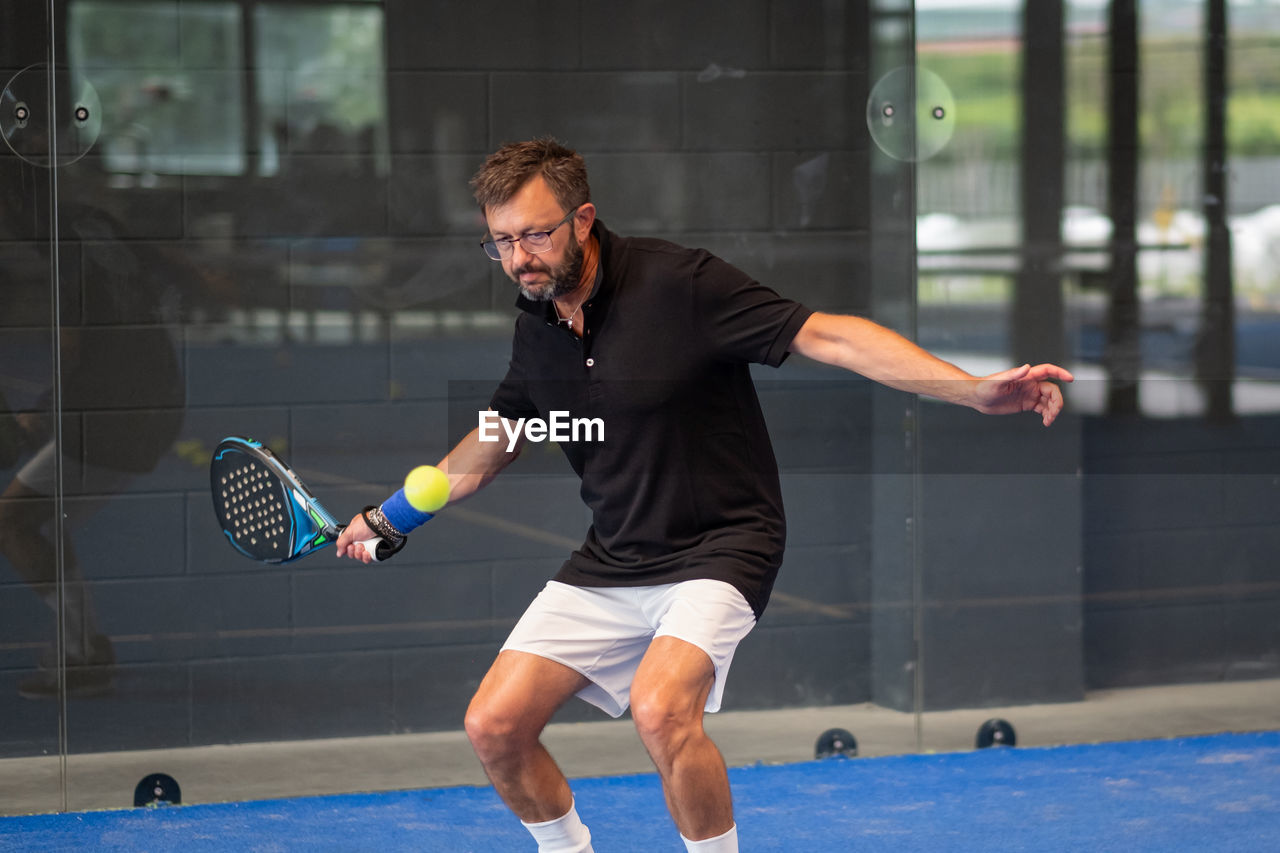 Man playing padel in a blue grass padel court indoor - young sporty boy padel player hitting ball 