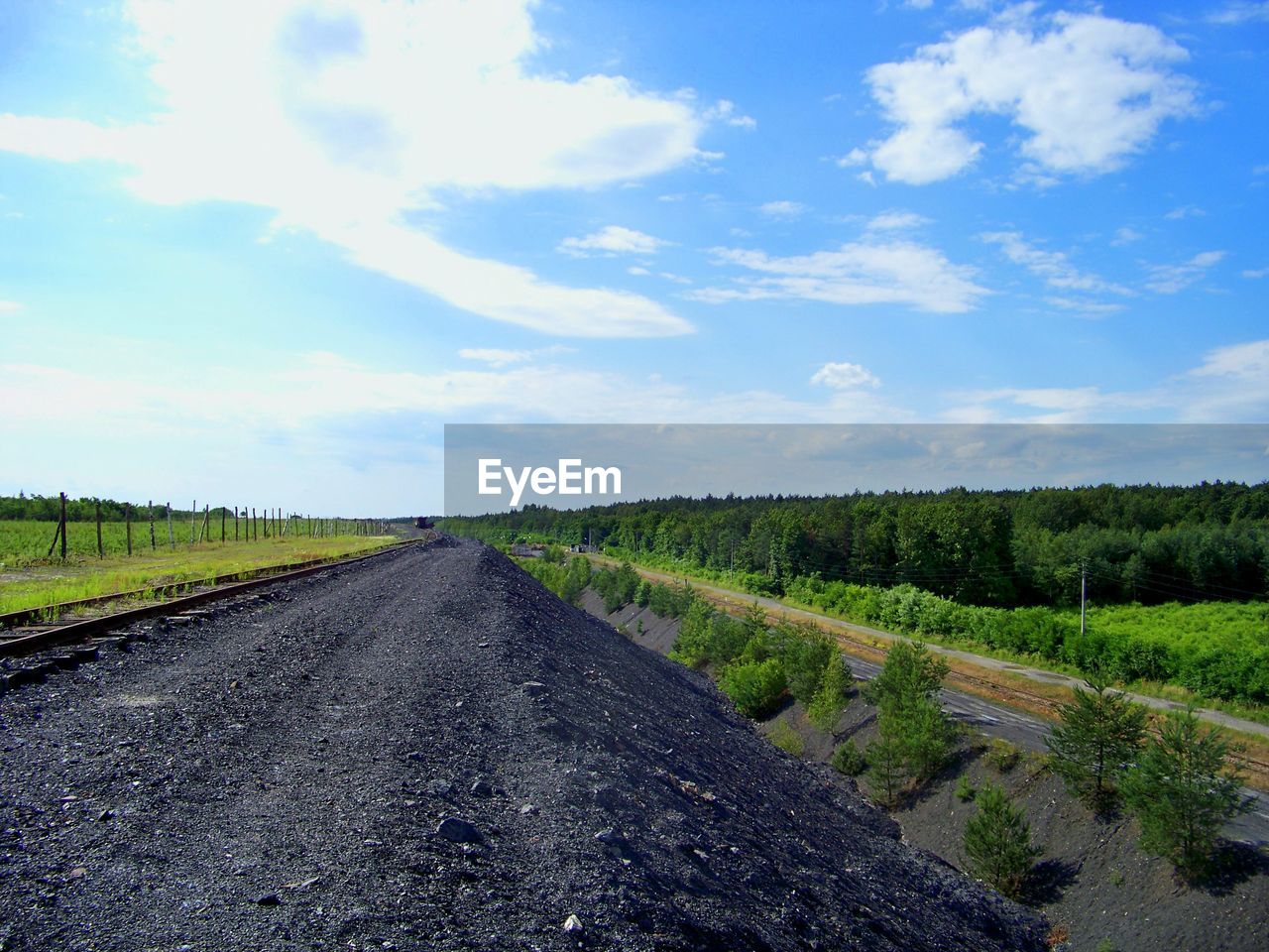 Railroad track on slag by field against sky