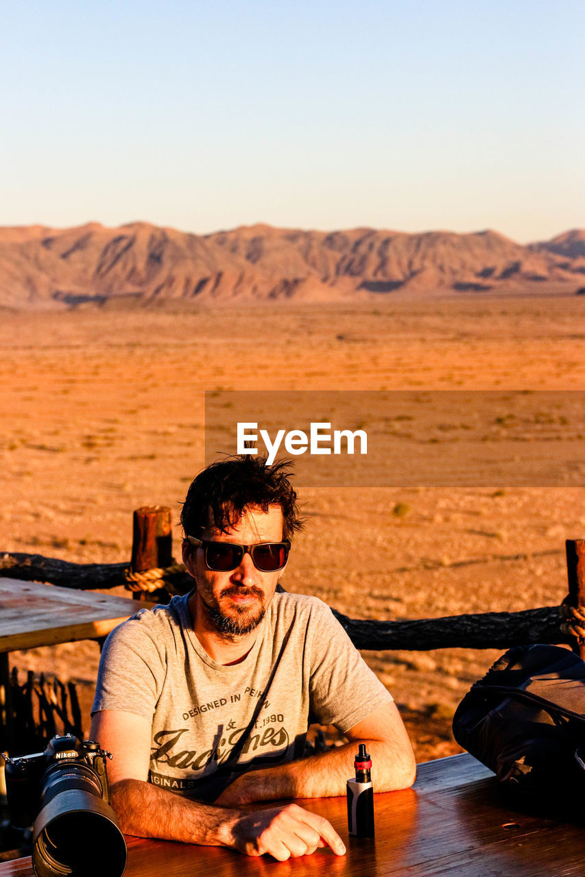 Portrait of man sitting against landscape and sky