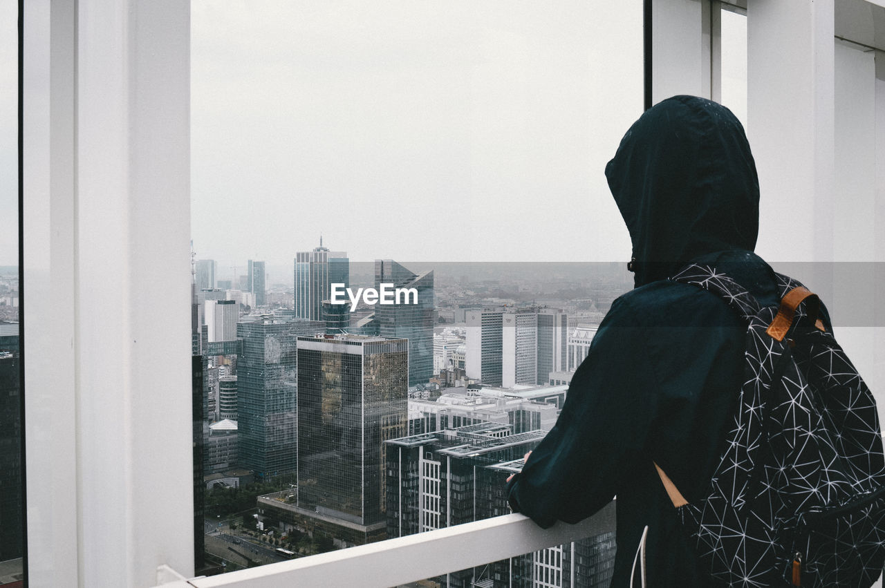 Rear view of man looking at cityscape through window