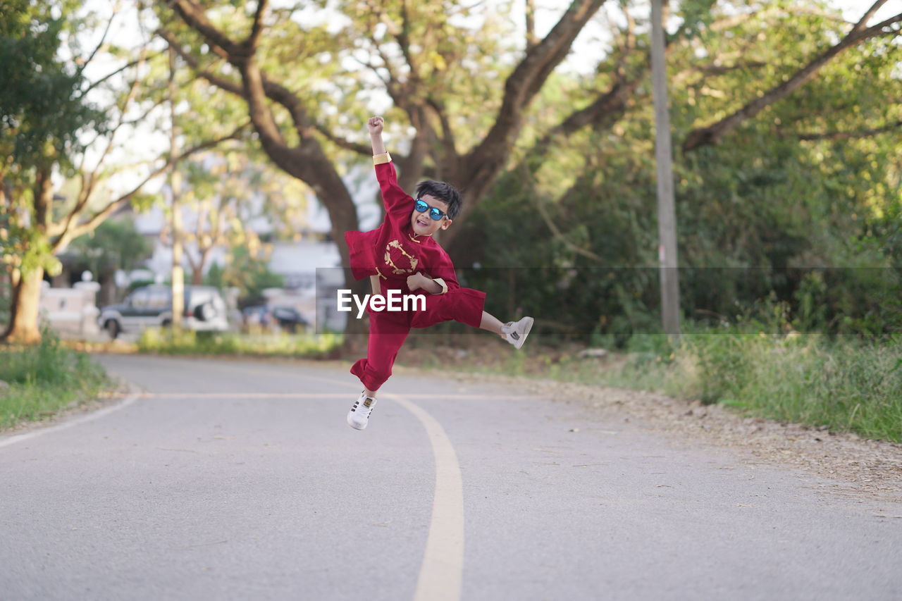 GIRL JUMPING ON ROAD AGAINST TREES