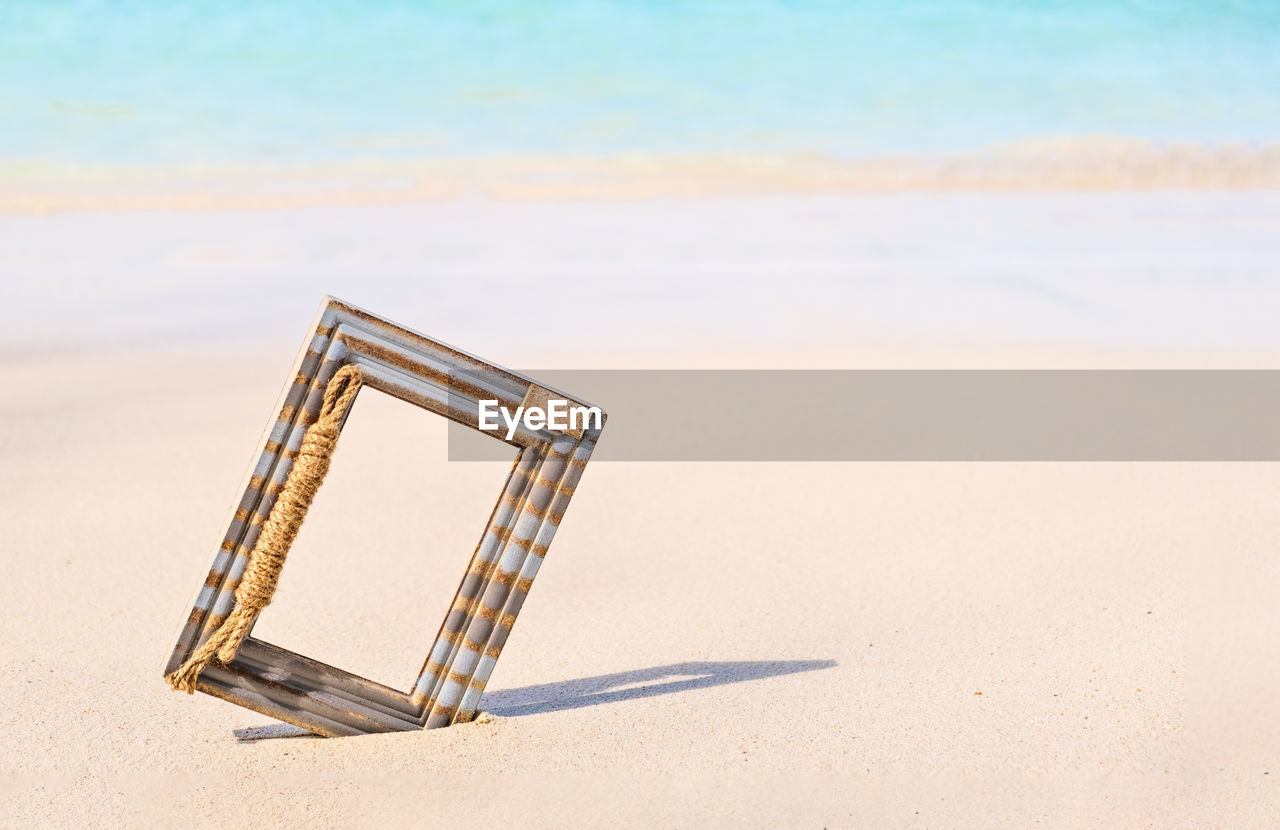 Wooden photo frame on the tropical sea sand and the beach background with copy space