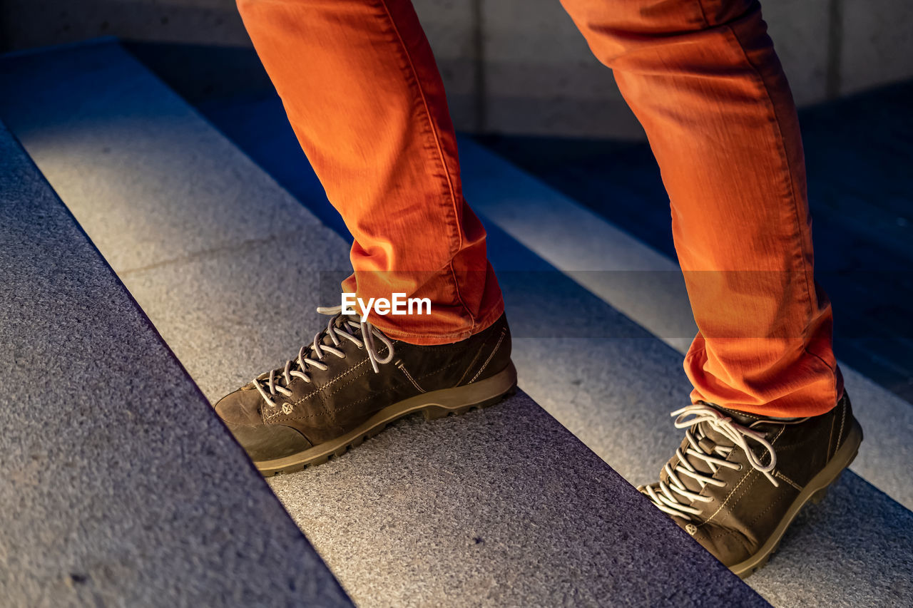 Male legs in walking boots and red jeans climb the illuminated stone steps on a winter evening