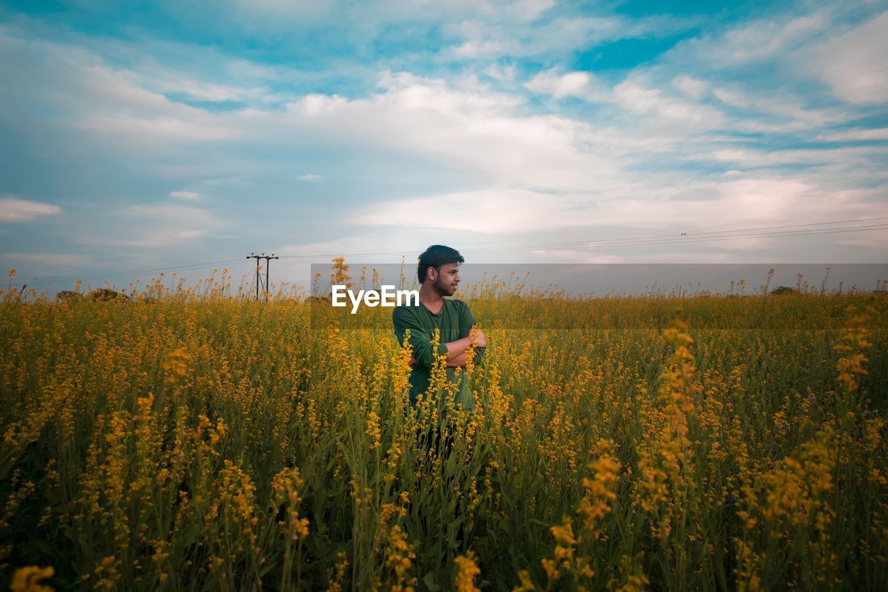 Thoughtful man standing at rape field against cloudy sky