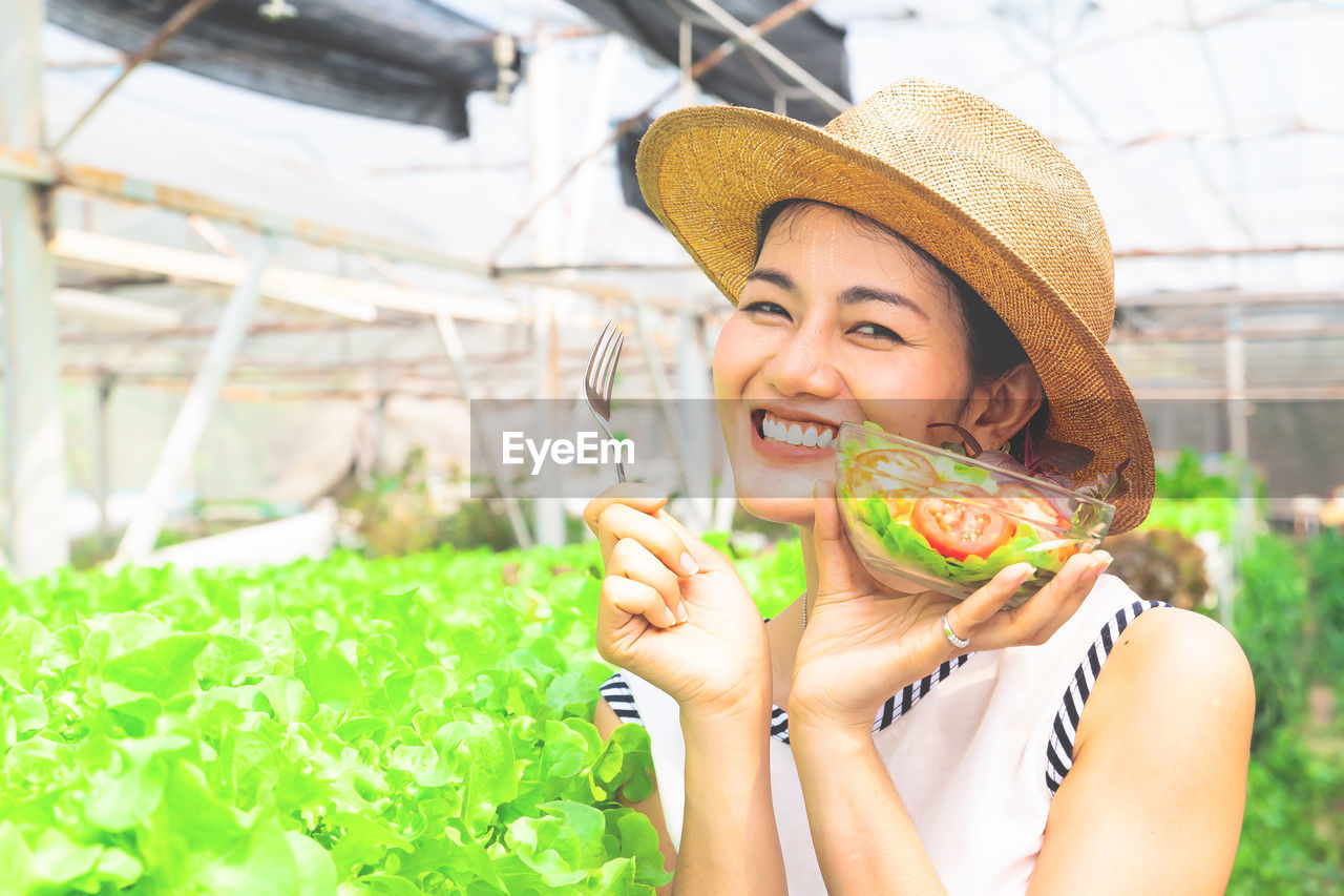 Portrait of smiling woman holding salad bowl in greenhouse