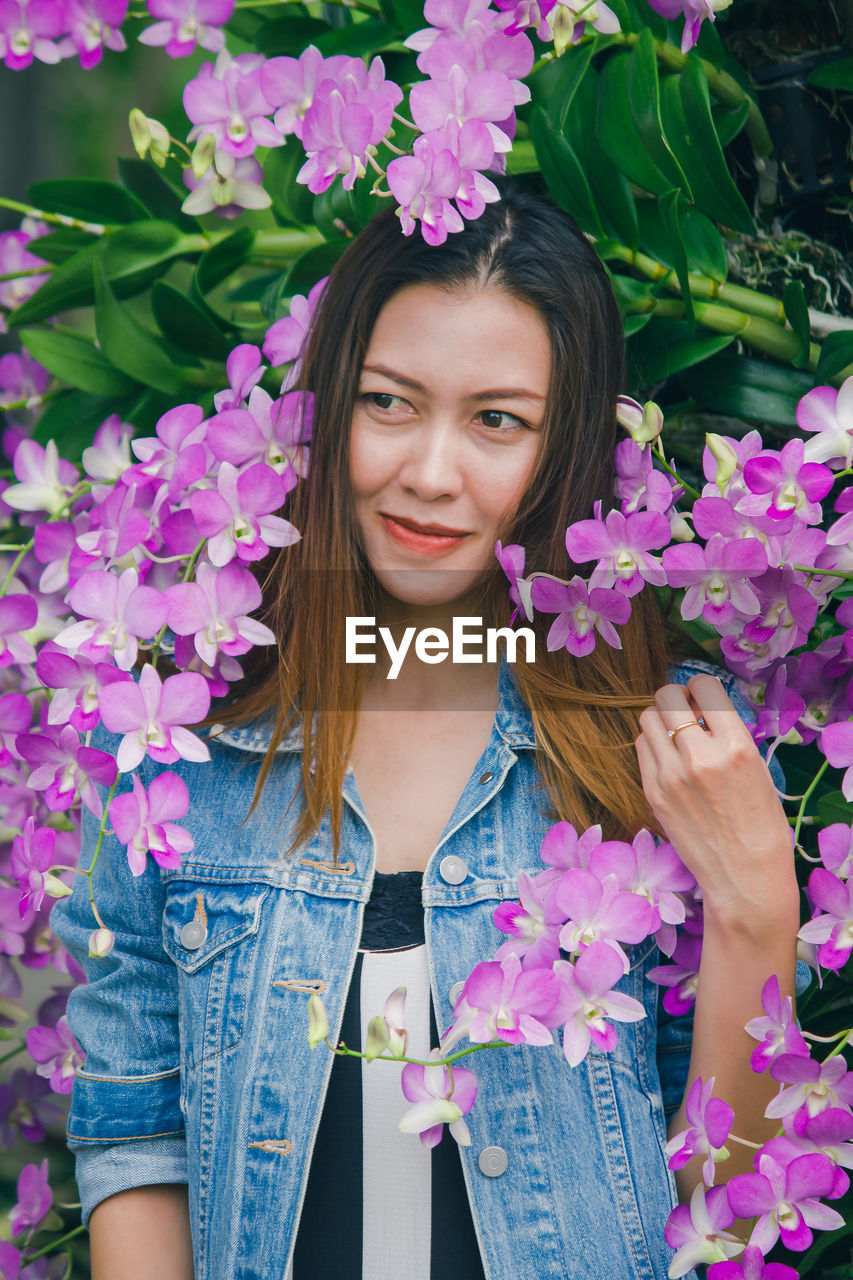 PORTRAIT OF BEAUTIFUL YOUNG WOMAN STANDING BY PINK FLOWER