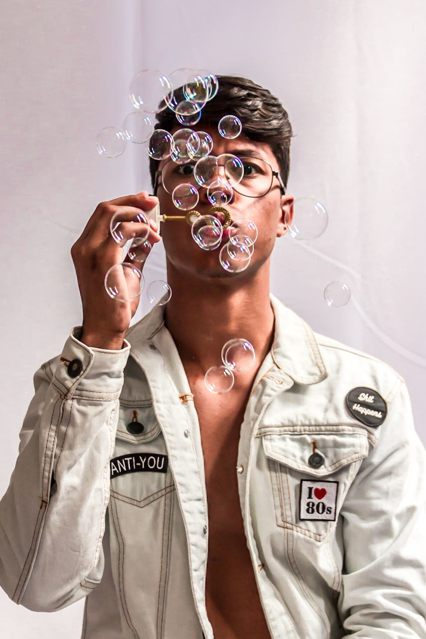 Young man blowing bubbles against wall