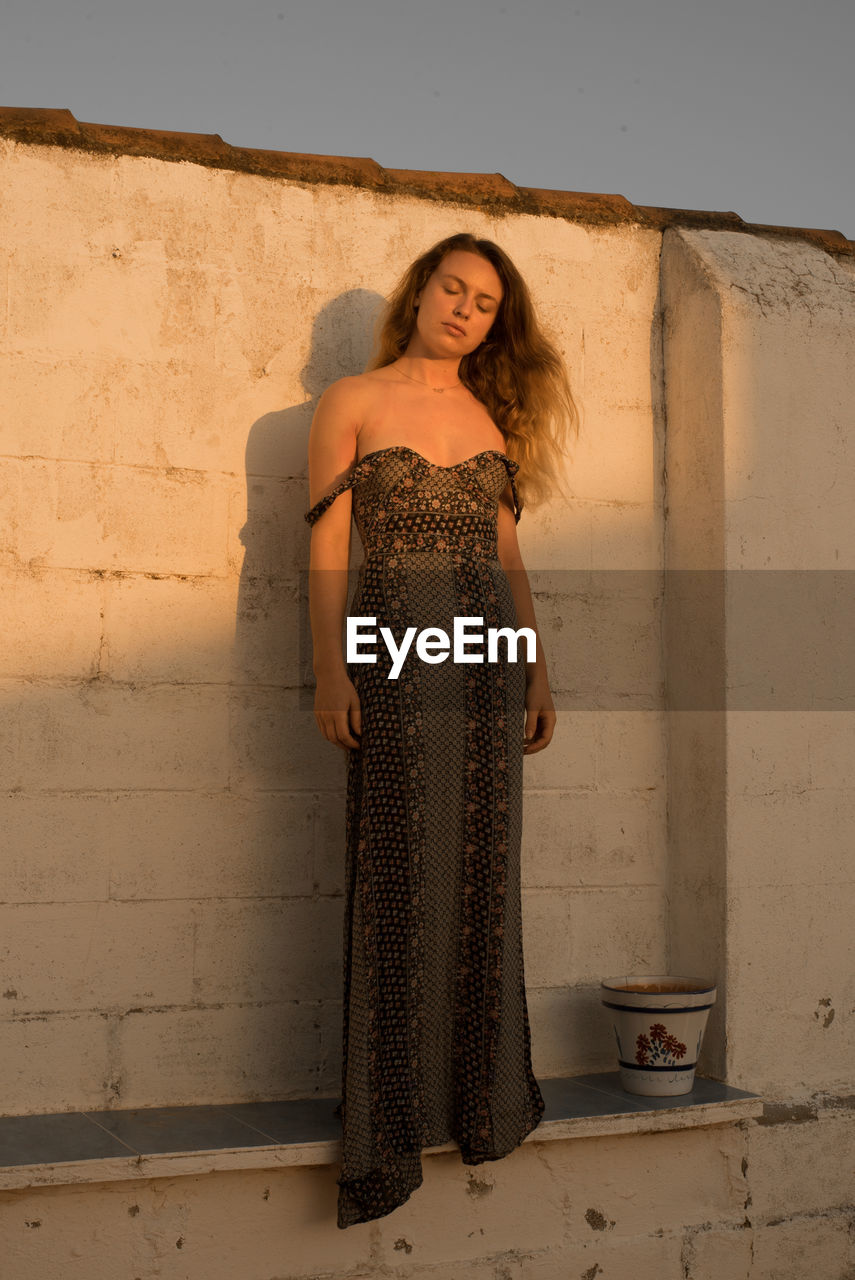 PORTRAIT OF BEAUTIFUL YOUNG WOMAN STANDING AGAINST WALL