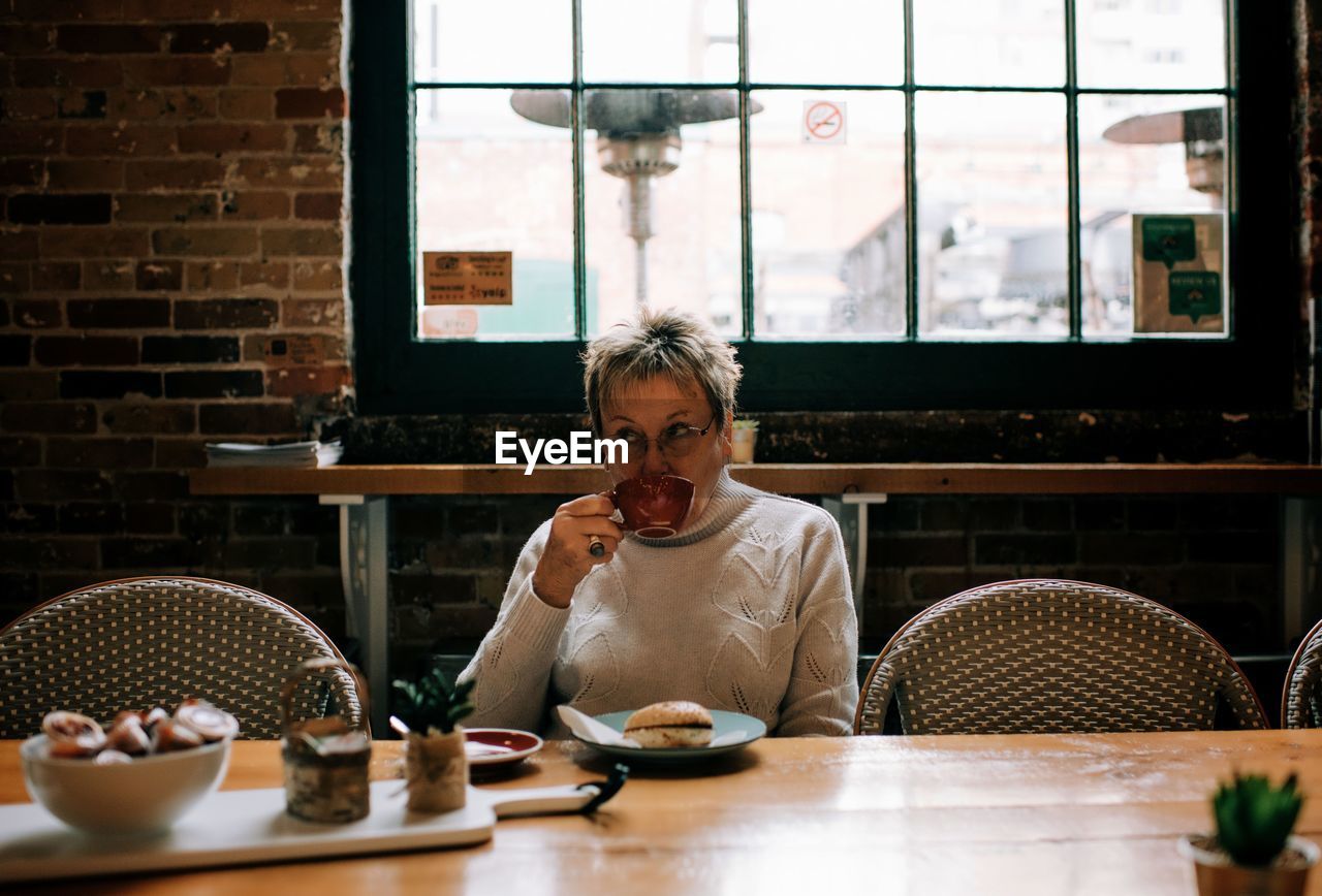 Woman sipping coffee in a cafe and eating bagel