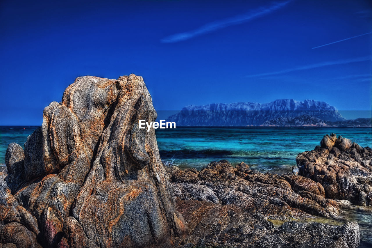 Rock formation on beach against blue sky