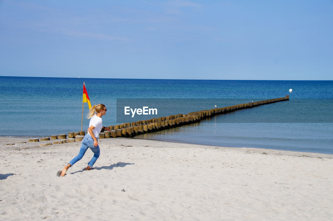 Full length of woman running on beach against sky