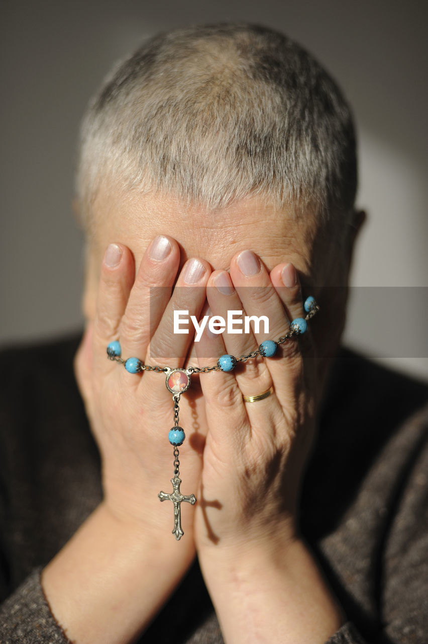 Mature woman with a rosary in her hands and short hair covering her face