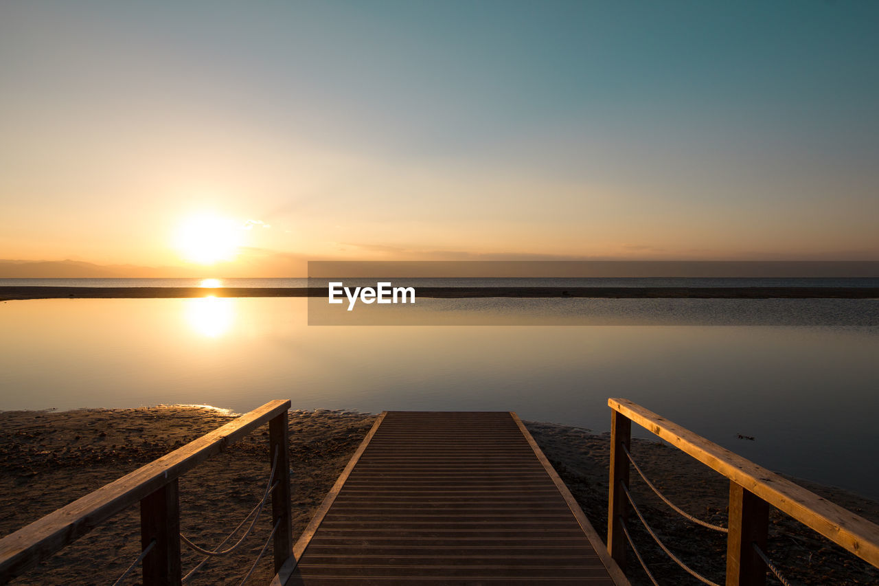 PIER AMIDST SEA AGAINST SKY DURING SUNSET
