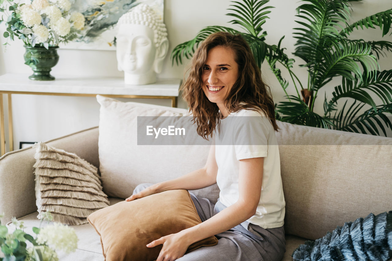 Cheerful woman sits at home on the sofa hugging a pillow.