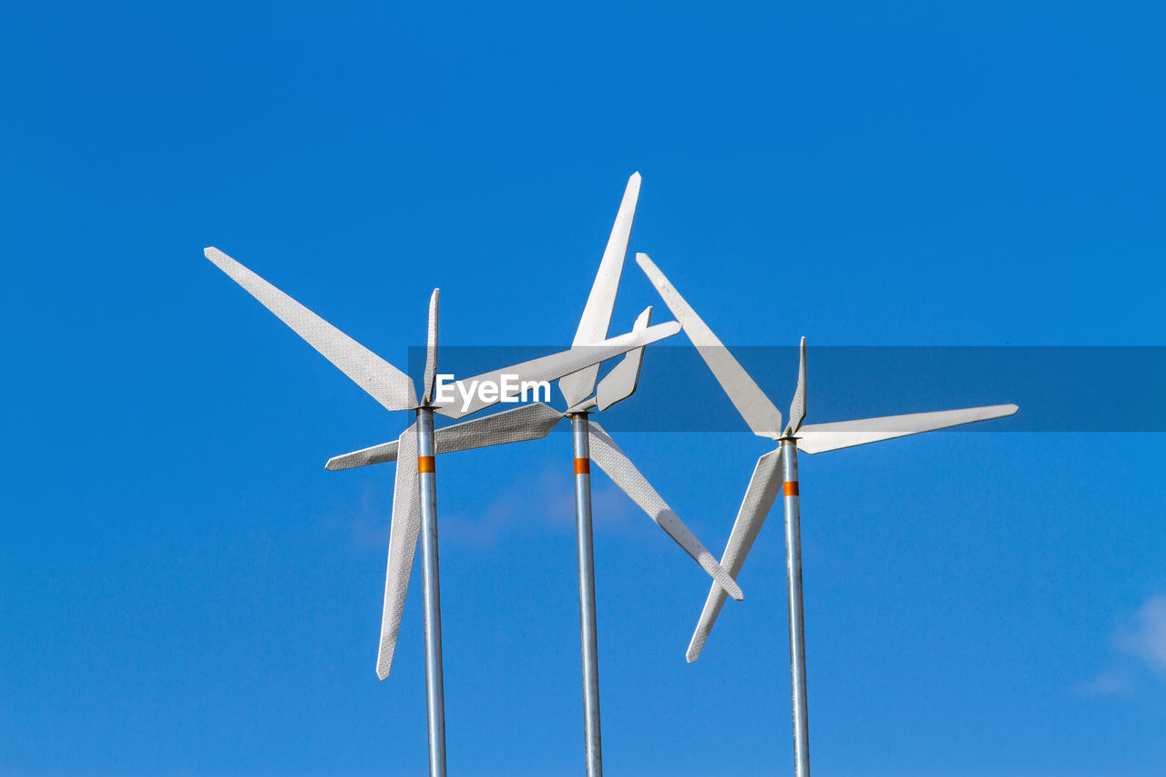 White wind turbines producing alternative energy on blue sky