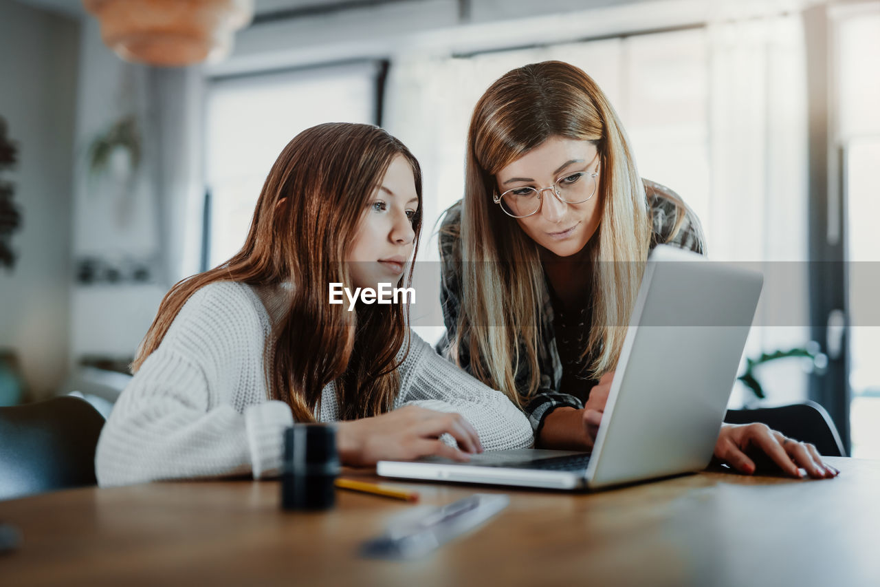 Mother assisting daughter in using laptop on table at home